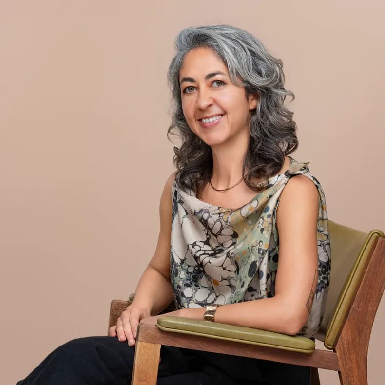 Modern corporate headshot seated against a warm neutral studio background