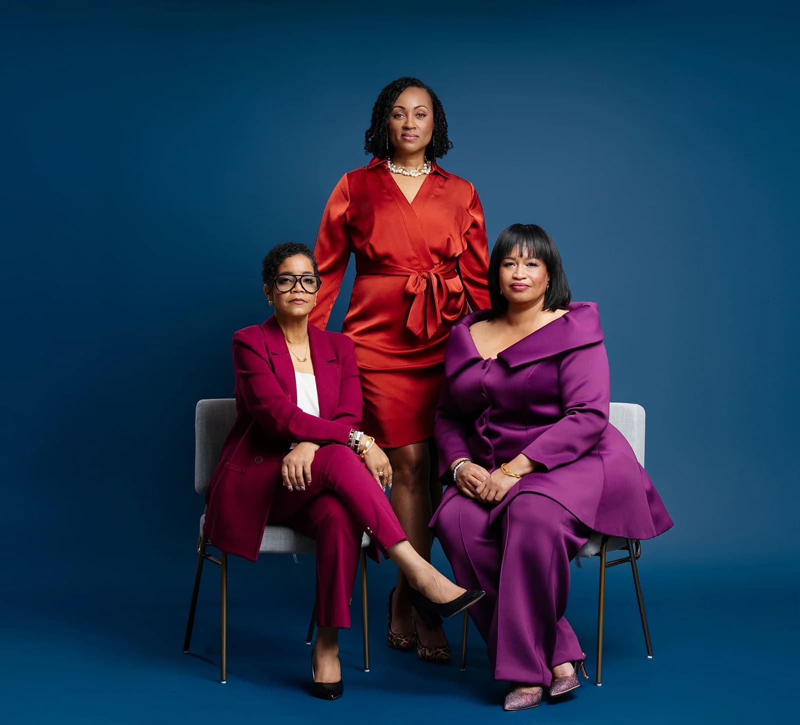 Three professionals in colorful suits posed against a deep blue studio backdrop