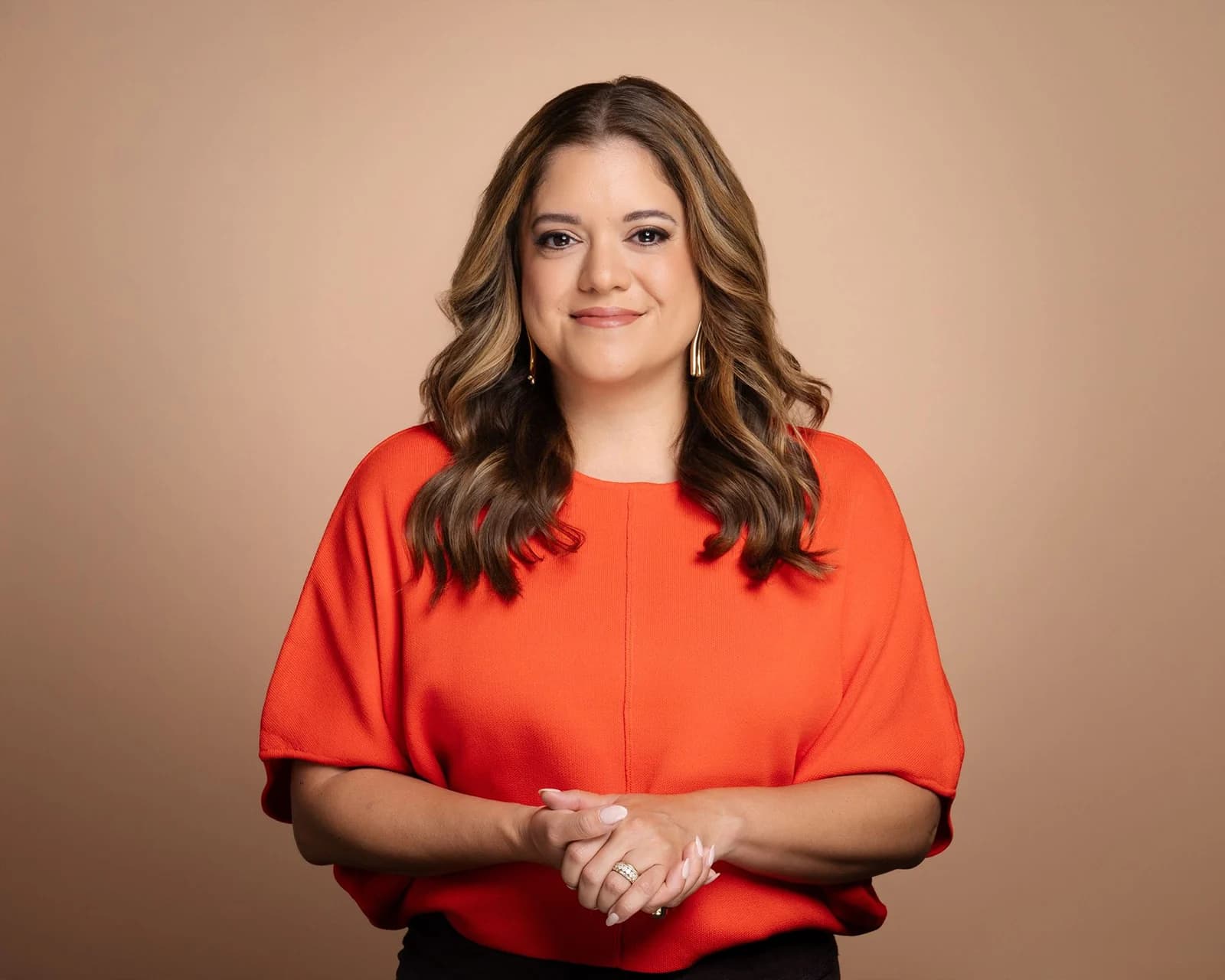 Woman in a red-orange blouse photographed against a warm neutral studio backdrop