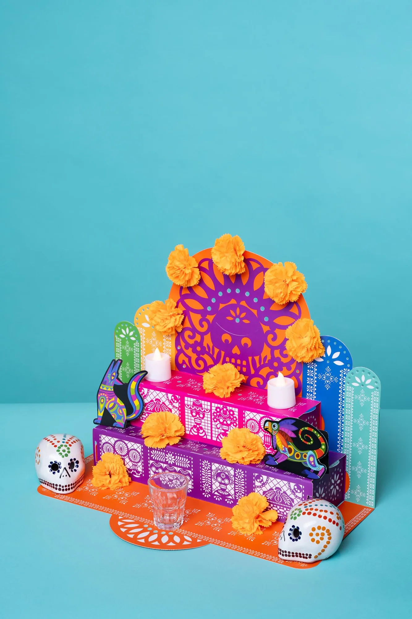 Colorful miniature altar with marigolds and sugar skulls against a turquoise backdrop